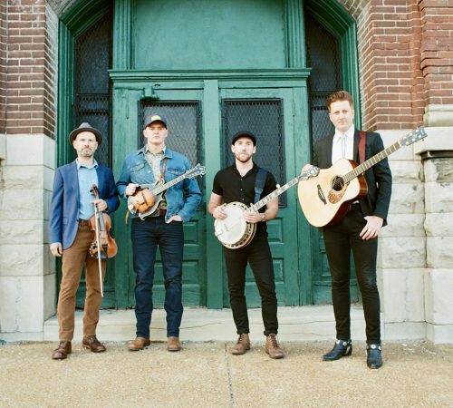 Bluegrass meets Irish with JigJam Four musicians standing in front of a brick building with a green door, holding instruments