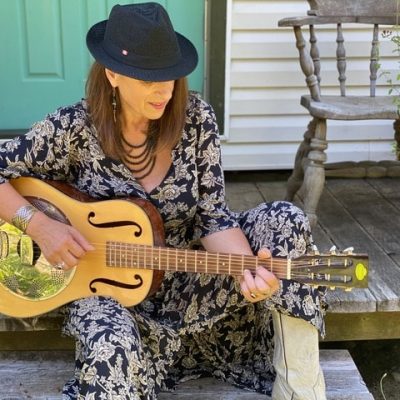 A picture of Marianne Grittani sitting on a porch playing a guitar