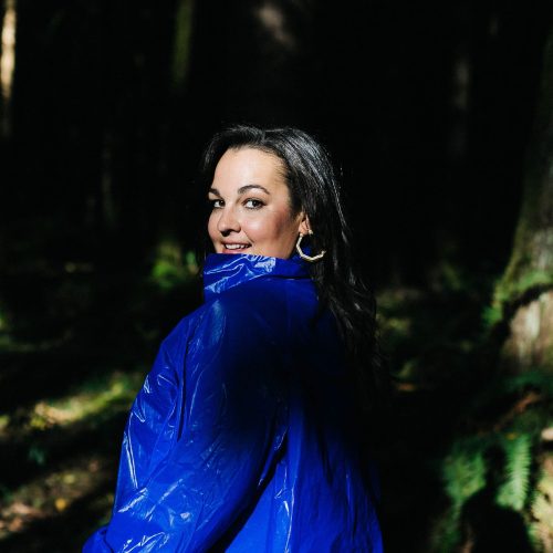Naomi Shore standing in forest with blue jacket on