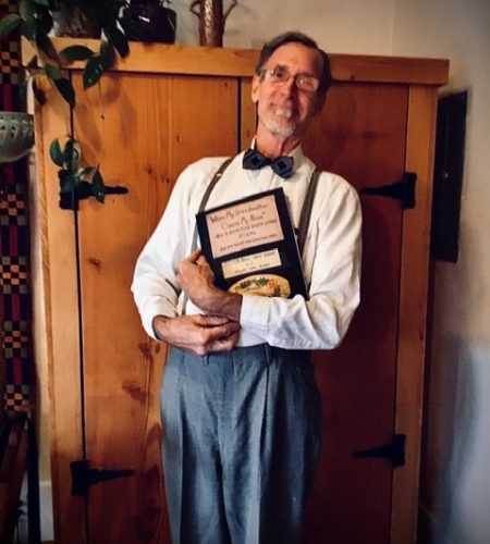 Peter Paul Van Kamp standing in front of a wooden armoire holding a homemade book