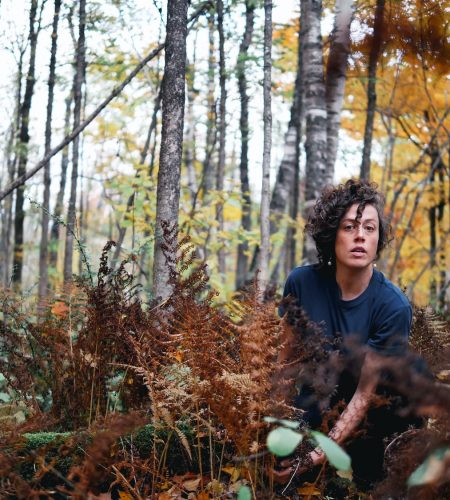 Rachael Kilgour in a forest, sitting on a downed forest log in a autumn like setting in the background