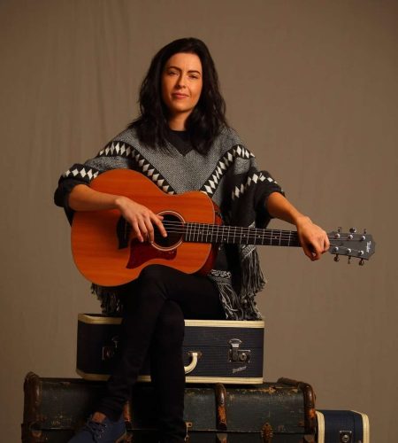 Christy Vanden sitting on a group of suitcases holding her guitar.